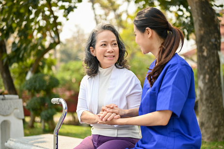 Vietnamesische Pflegekraft hält Seniorin die Hand